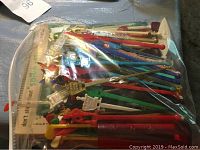 Plastic bag containing multiple colorful vintage swizzle sticks with various designs and shapes on top.