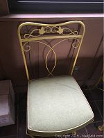 Single yellow wrought iron patio chair with green cushioned seat, decorative back featuring leaf motif.