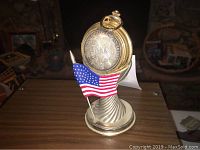 Pocket watch with silver dollar design displayed on a stand featuring an American flag.