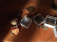 View of cufflinks and tie tacks on wood surface showing different styles, some in clear cases