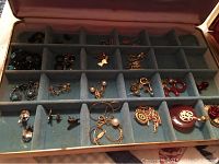 Blue velvet-lined jewelry box with rows of small compartments holding earrings, pearl earrings, clip-ons, and chains.