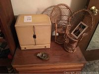 Cream jewelry box closed with two small wicker chairs and metal shell dish on wooden surface