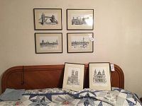 Six framed black and white London scene prints hung and positioned over a bed with a wooden headboard.