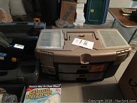 Photo showing large plastic toolbox with top compartments and attached drawers, Ryobi circular saw partially visible on left corner, Glass Wizard cleaning kit box in front.