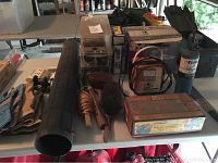 Overview of items on table including gloves, wire brushes, black tool case, plastic storage boxes, charger boxed items