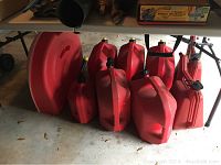 Red plastic gas cans of varying sizes and shapes on floor under table