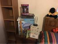 Wide view of the miscellaneous lot showing tall wooden shelf, boxed items including Furby, foot spa box, and other boxes placed on furniture