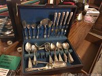 Wooden chest open to reveal blue felt-lined storage with repousse sterling silver flatware displayed