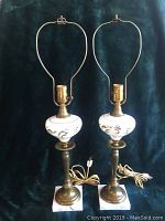 Full view of pair of porcelain and brass table lamps with marble bases and attached power cords.