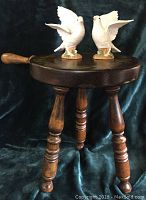 Wooden stool with two white ceramic birds posed on top, showing turned legs and handle.