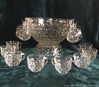 Image showing the full punch set with punch bowl and 12 matching cups arranged around it on a dark fabric background.