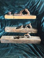 Three antique wooden hand planes stacked, showing overall condition and size differences