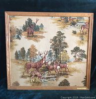 Full view of vintage fabric picture in oak frame showing deer and forest landscape.