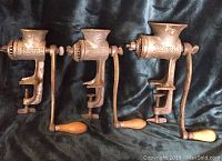 Three Universal brand manual meat grinders shown side by side on black fabric, each with clamp base and hand crank with wooden handle.