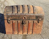 Front view of the closed antique dome top trunk showing rusty metal straps and decorative hardware.