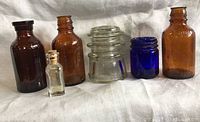 Front view of all bottles and the clear glass insulator arranged in a row showing color and size differences