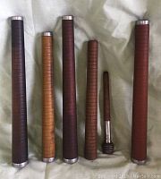 Photo of all six yarn spindles standing upright showing differences in height and wood color with metal caps at ends.