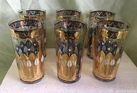 Photo of six vintage George Briard drink glasses with gold and black patterns arranged in two rows of three on a white surface.