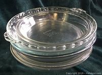 Stack of six clear glass Pyrex pie dishes showing the fluted edge and smooth edges in profile.