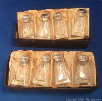 Two open boxes each containing four clear glass salt and pepper shakers with sterling silver tops, arranged in satin-lined boxes.