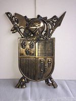Front view of metal medieval style shield wall plaque showing detailed heraldic symbols and helmet with spear design