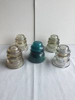 Five glass insulators displayed, three clear, one green, various sizes and shapes.