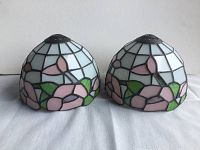 Pair of dome-shaped leaded glass lamp shades with floral pink and green stained glass pattern on a white background on fabric surface.