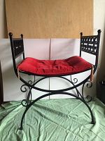 Full view of the vintage wrought iron bench with curved seat and red cushion on top, showing its structure and design.