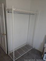 Full view of white metal clothing rack showing top wire shelf, hanging rod and bottom wire shelf.