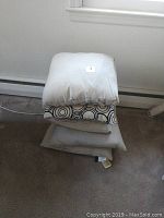 Stack of five assorted throw pillows in beige and patterned with some stains visible