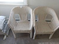 Two white wicker chairs side by side on carpeted floor under window, showing overall front and side view
