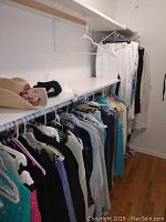 View of women's clothing hanging on rack with hats on upper shelf, including white pants and various tops