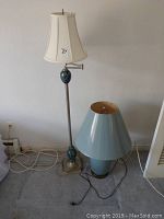 Silver floor lamp with white fabric shade and blue ceramic accents on pole, next to blue table lamp with matching shade on floor.