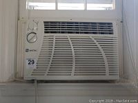 Front view of Maytag window air conditioner installed in a window, showing the grille and control dials.