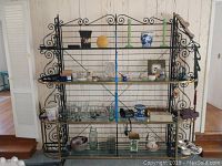 Full front view of the bakers rack showing overall design with black metal frame and brass accents. Glass shelves hold various items (not included).