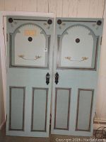 Front view of two blue faux doors with decorative gold and black painted borders and floral designs, showing full door panels and faux hardware.