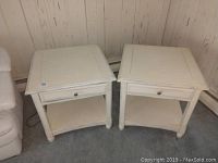 Two matching white wooden side tables placed side by side, showing overall condition and size relative to surrounding area.
