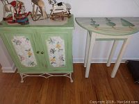 Front view of green floral painted cabinet and shrub top side table side by side on wooden floor.