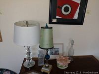 Photo showing two tall glass ball lamps with white and green shades, crystal and glass decanters, pig bowl, and other small decorative items on a table