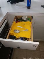 Open drawer showing a silver serving spoon atop a yellow napkin along with various miscellaneous kitchen items.