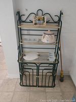 Front view of green and gold metal bakers rack with contents on shelves but not included in sale.