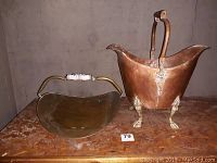 Side view of copper claw foot pail next to brass log holder on wooden surface with number 79 label.