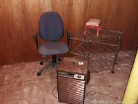 Photo showing overall lot: blue-gray rolling office chair, small red wooden stool on top of black metal corner rack, and Fedders dehumidifier in front