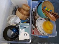 Two large bins showing an assortment of wooden bowls, plates, a butter dish, salad servers, and various kitchen and household items.
