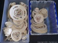Two blue plastic bins filled with Wedgwood Corinthian dinnerware, including stacks of plates and cups, showing detailed multi-colored floral and bird designs on white porcelain.