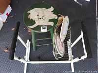 Overall view showing green painted stool with white dog illustration, white metal mobility aid, white stool with floral plates and two decorative small signs.