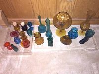 Photo of assorted vintage molded glass vases and novelty glass items in amber, blue, red, and green colors arranged on a floor against wooden paneling