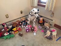 Wide shot of all stuffed animals in collection showing variety including large Dalmatian, Disney characters, Beanie Babies, and assorted plush toys on beige carpet floor near window and heater.