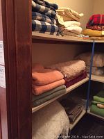 Multiple folded towels and linens stacked on wooden shelves in a storage space, showing some textured bath mats and bath towels in earth tones.