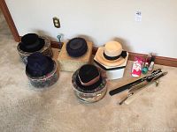 Four vintage ladies hats displayed on the floor with their original boxes, including floral patterned and plain cream colored boxes. Hats include black, navy, navy with decoration, and cream straw hat with black ribbon.